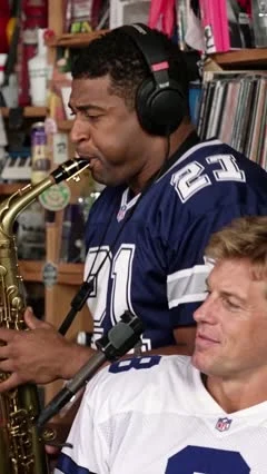 AI-generated Tiny Desk-style video frame of Deion Sanders playing saxophone